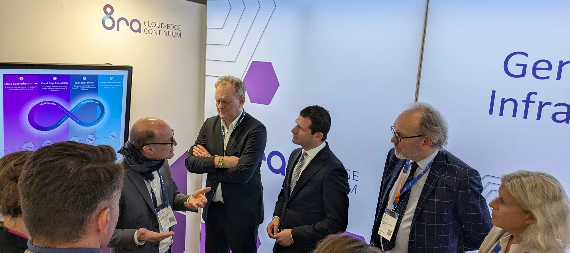 lively discussion between several people at the 8ra booth at MWC 2025